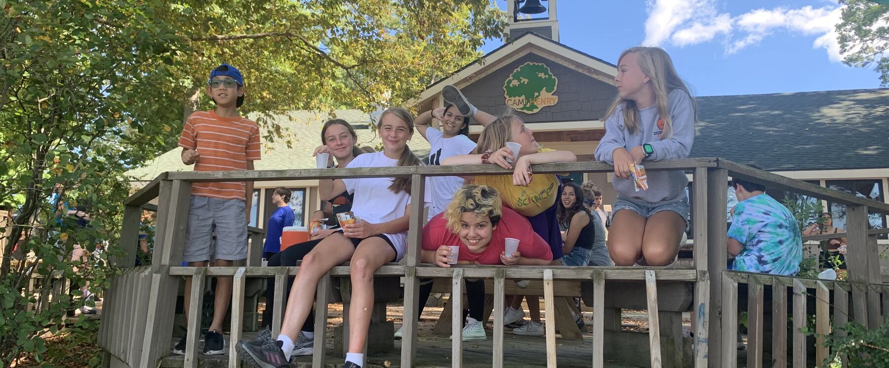 A group of middle school students sit on a deck and smile through the railings.