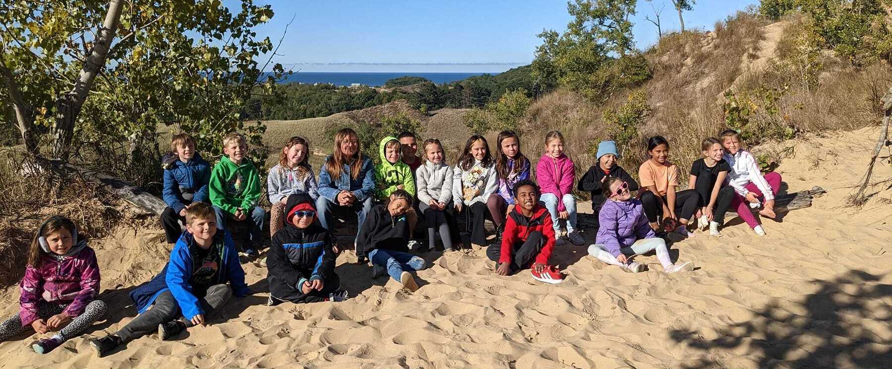 A group of 3rd grade students sit atop a dune