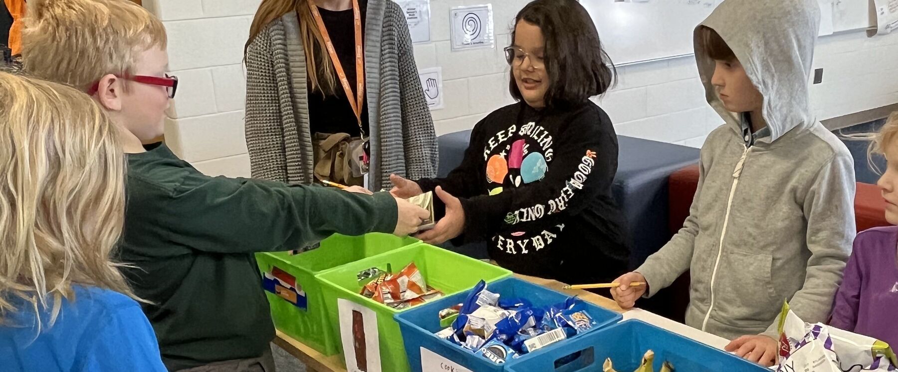 A first grade student pays for a snack at a snack table.